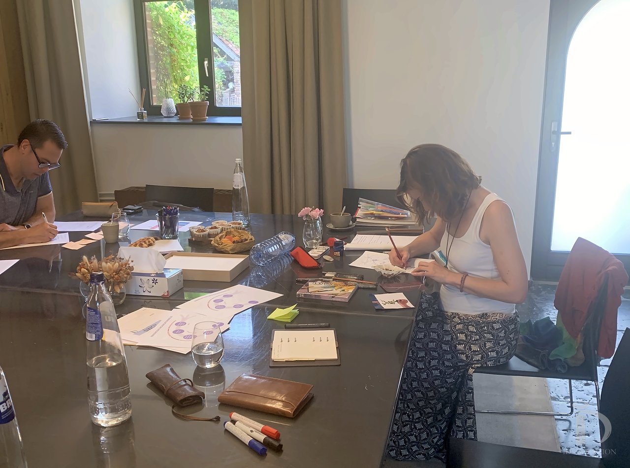 Aline Stukkens, assise à la grande table de l'atelier, guide un exercice d'écriture
